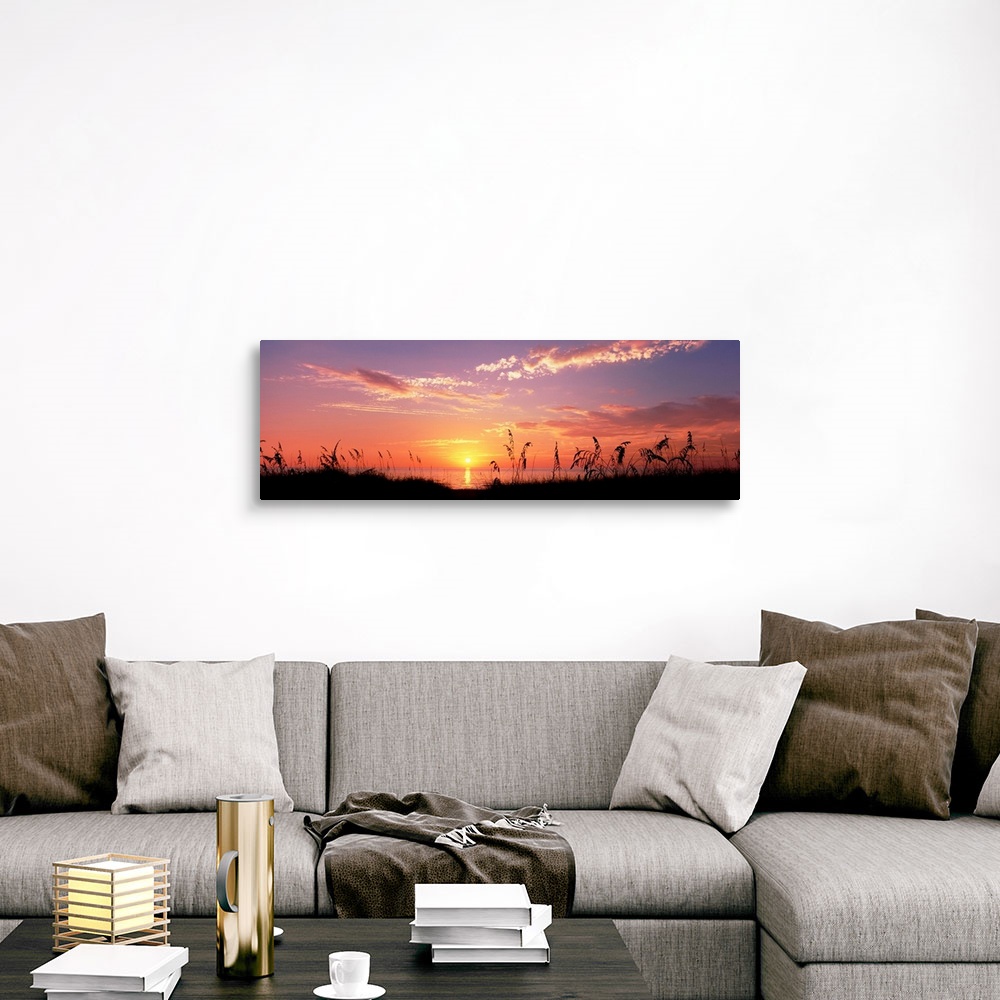 A traditional room featuring This wall art is a panoramic photograph of silhouetted sea grass in front of a calm sea at the en...