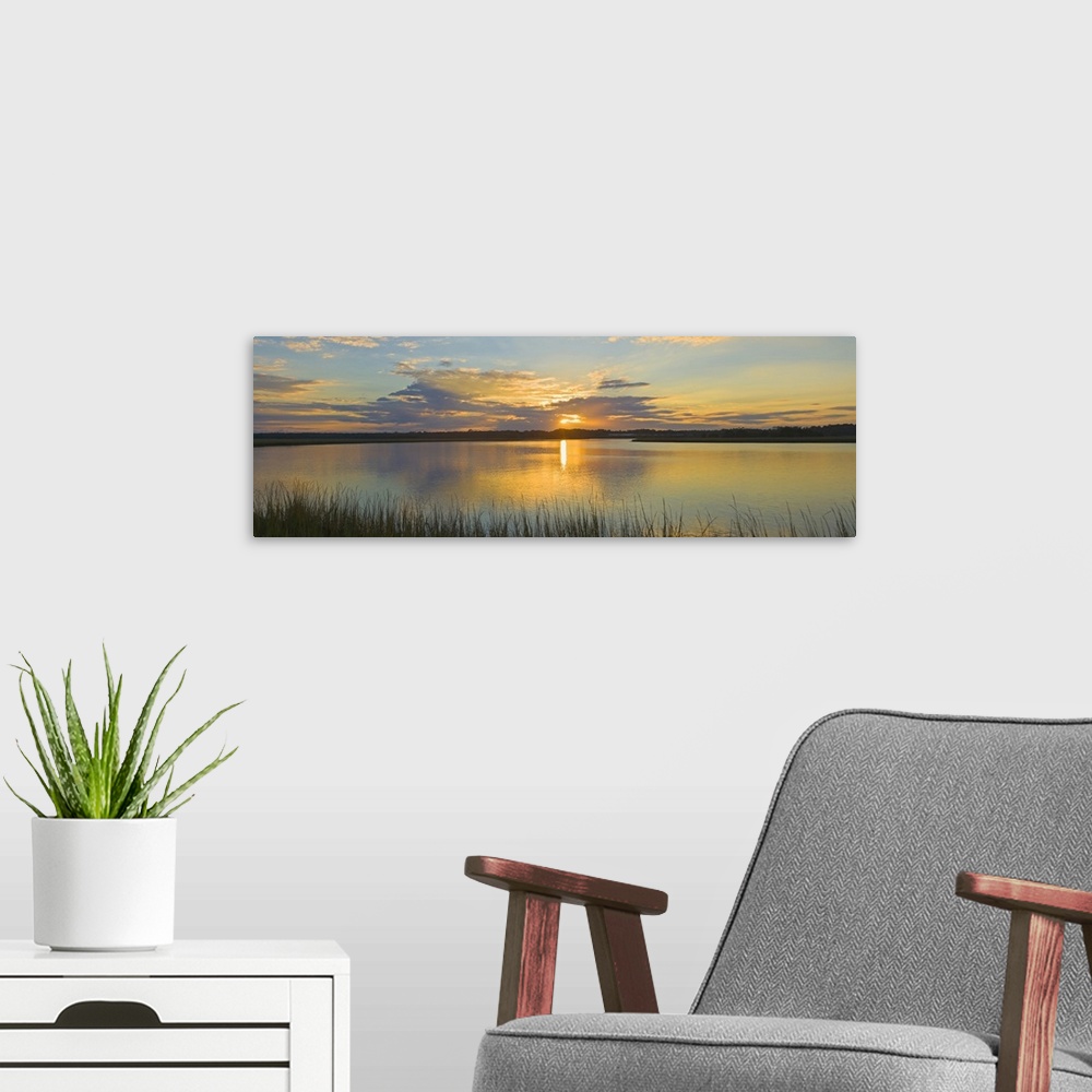 A modern room featuring Tall grass lines the bottom of this picture with a wide angle view of a body of water as the sun ...