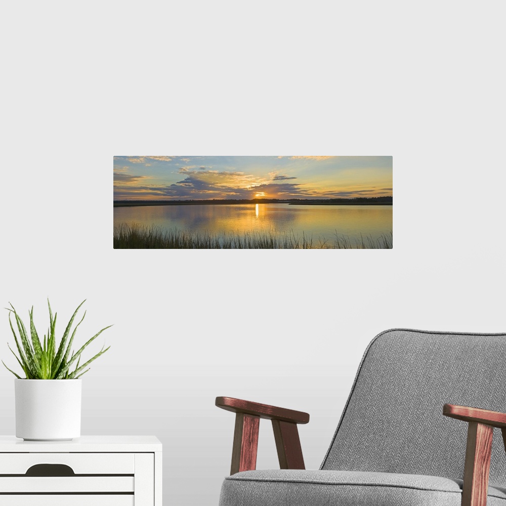 A modern room featuring Tall grass lines the bottom of this picture with a wide angle view of a body of water as the sun ...