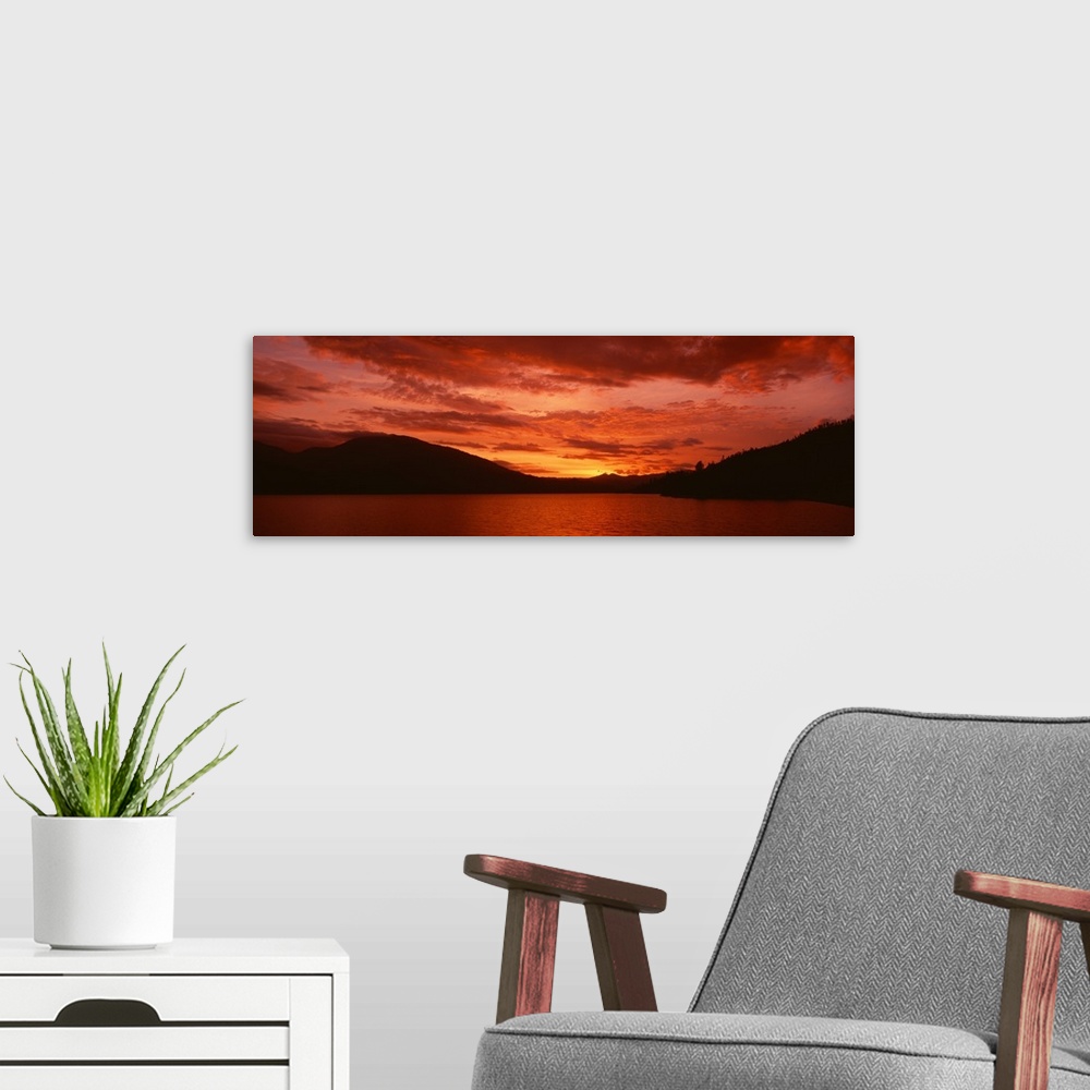 A modern room featuring Panoramic photograph of a vibrant fiery sunset over a silhouetted mountain landscape and Whiskeyt...