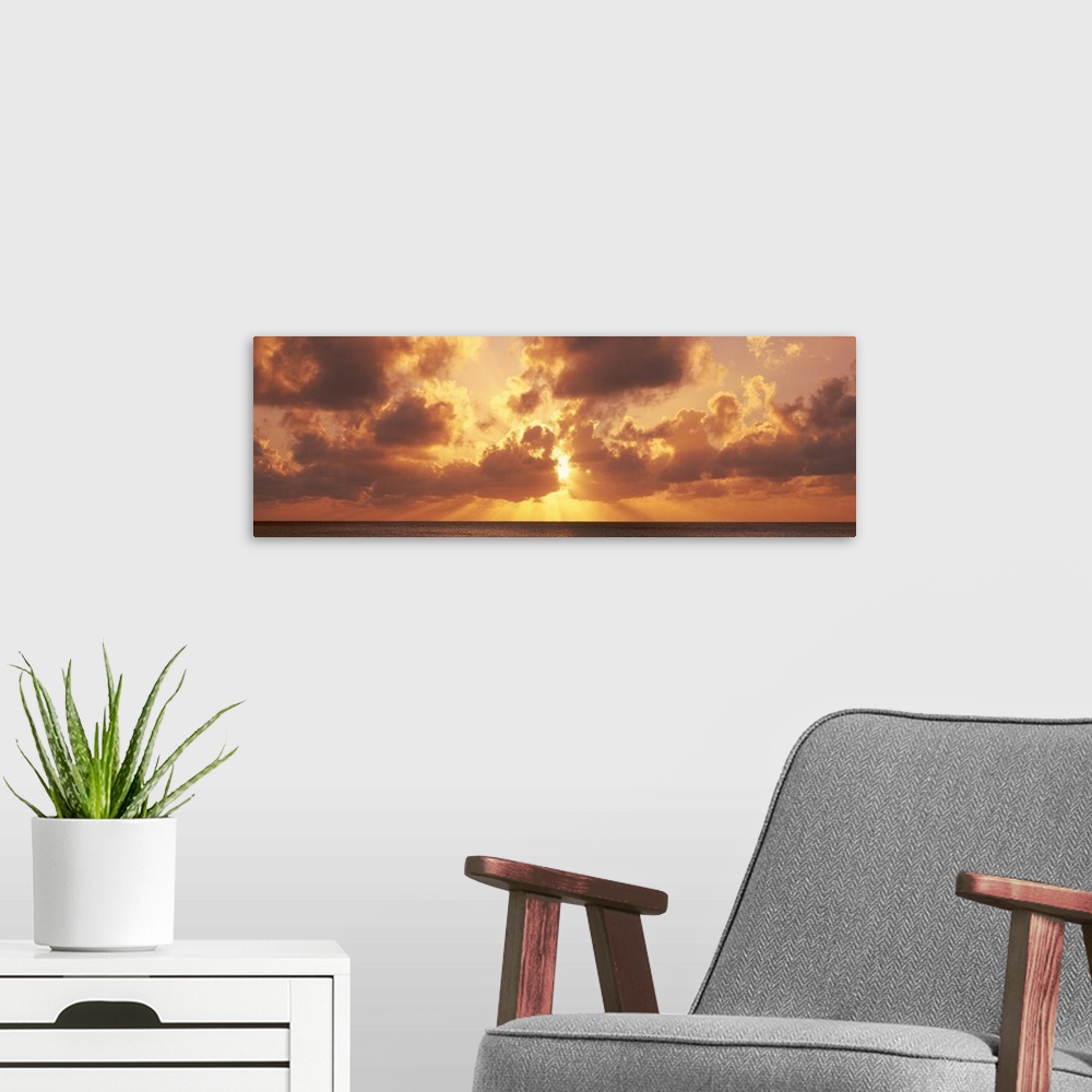 A modern room featuring Large panoramic photograph taken of a sunset behind the clouds with its rays bursting through and...