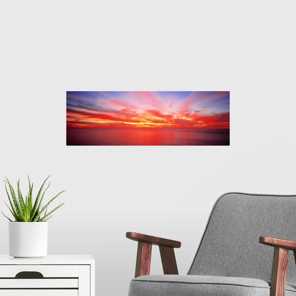 A modern room featuring Wide angle photograph on a giant wall hanging of the sky full of streaking clouds during a vibran...