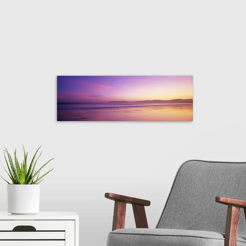 A modern room featuring This large panoramic piece shows a sun setting behind vast hills over the Pacific ocean.