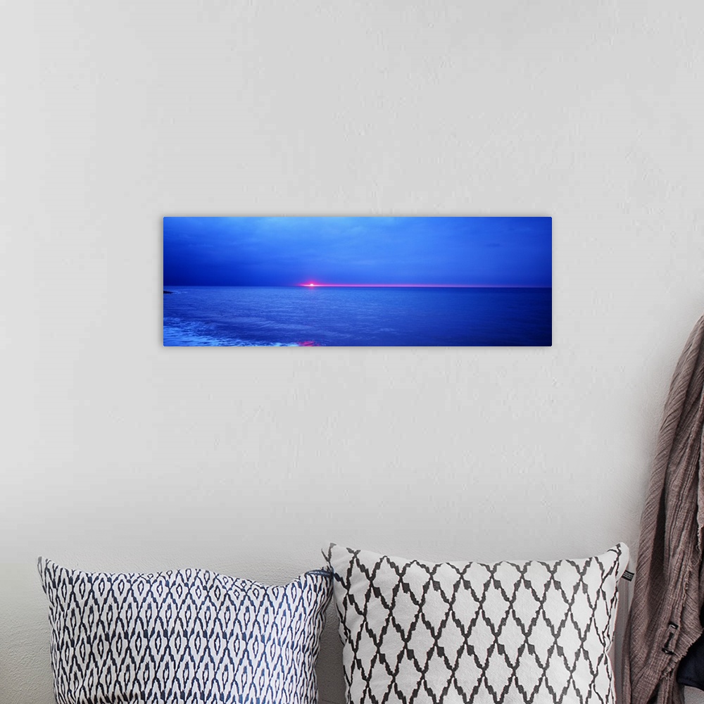 A bohemian room featuring Panoramic photograph of the sun setting just below the horizon over the vast blue ocean.