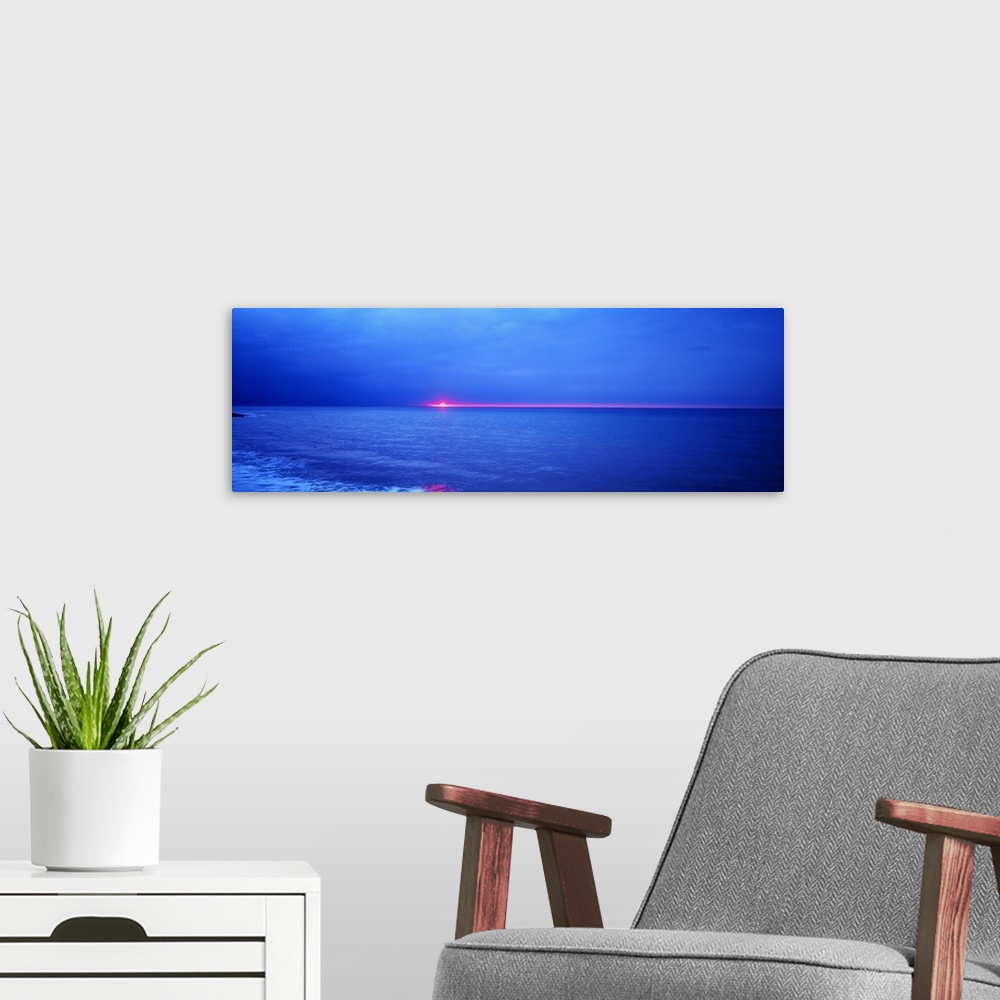 A modern room featuring Panoramic photograph of the sun setting just below the horizon over the vast blue ocean.