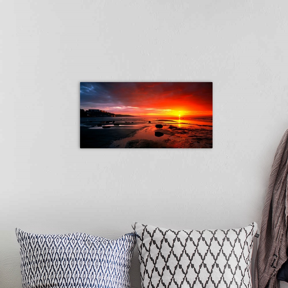 A bohemian room featuring Panoramic photograph that captures a colorful sunset on the shores of England.  The calm beach is...