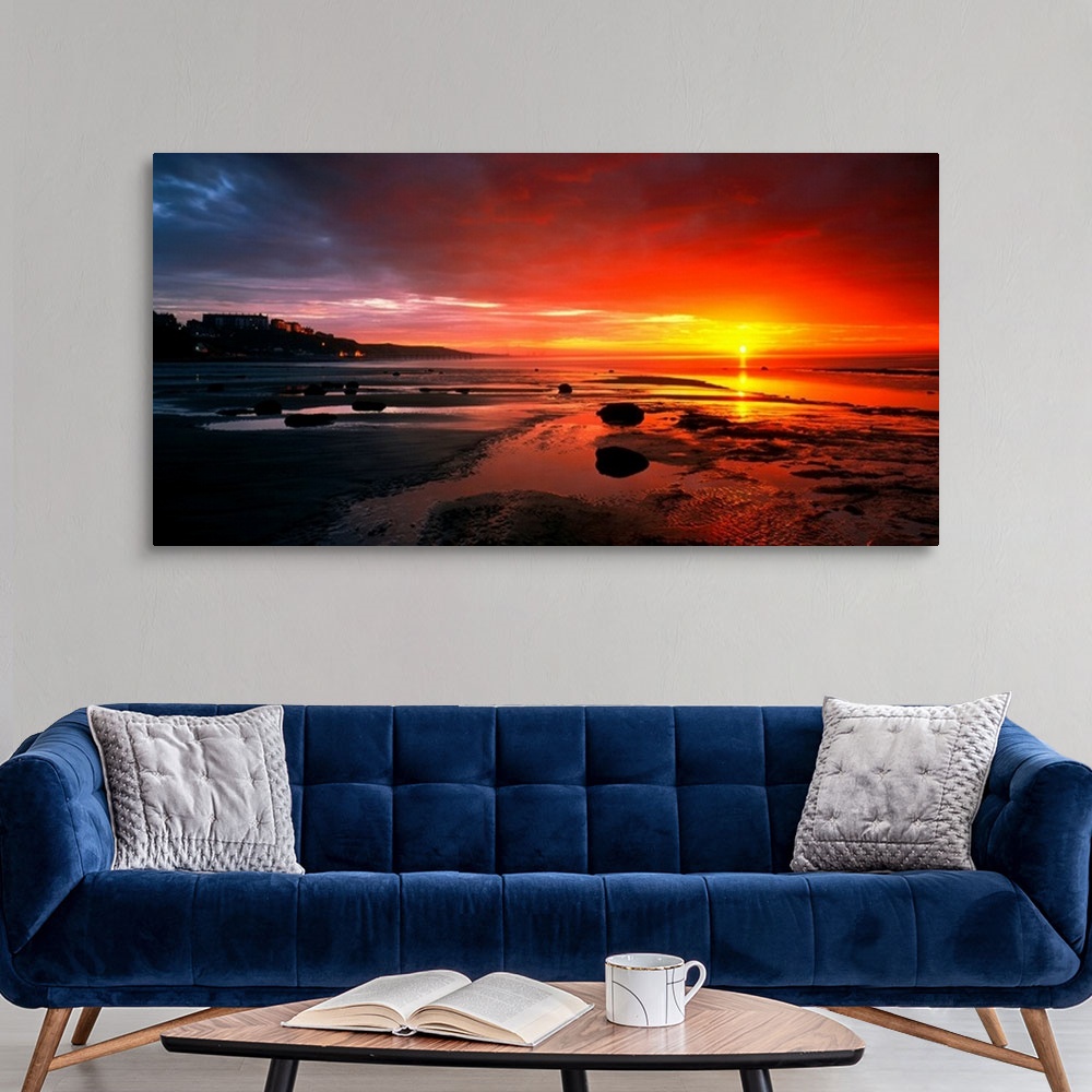 A modern room featuring Panoramic photograph that captures a colorful sunset on the shores of England.  The calm beach is...