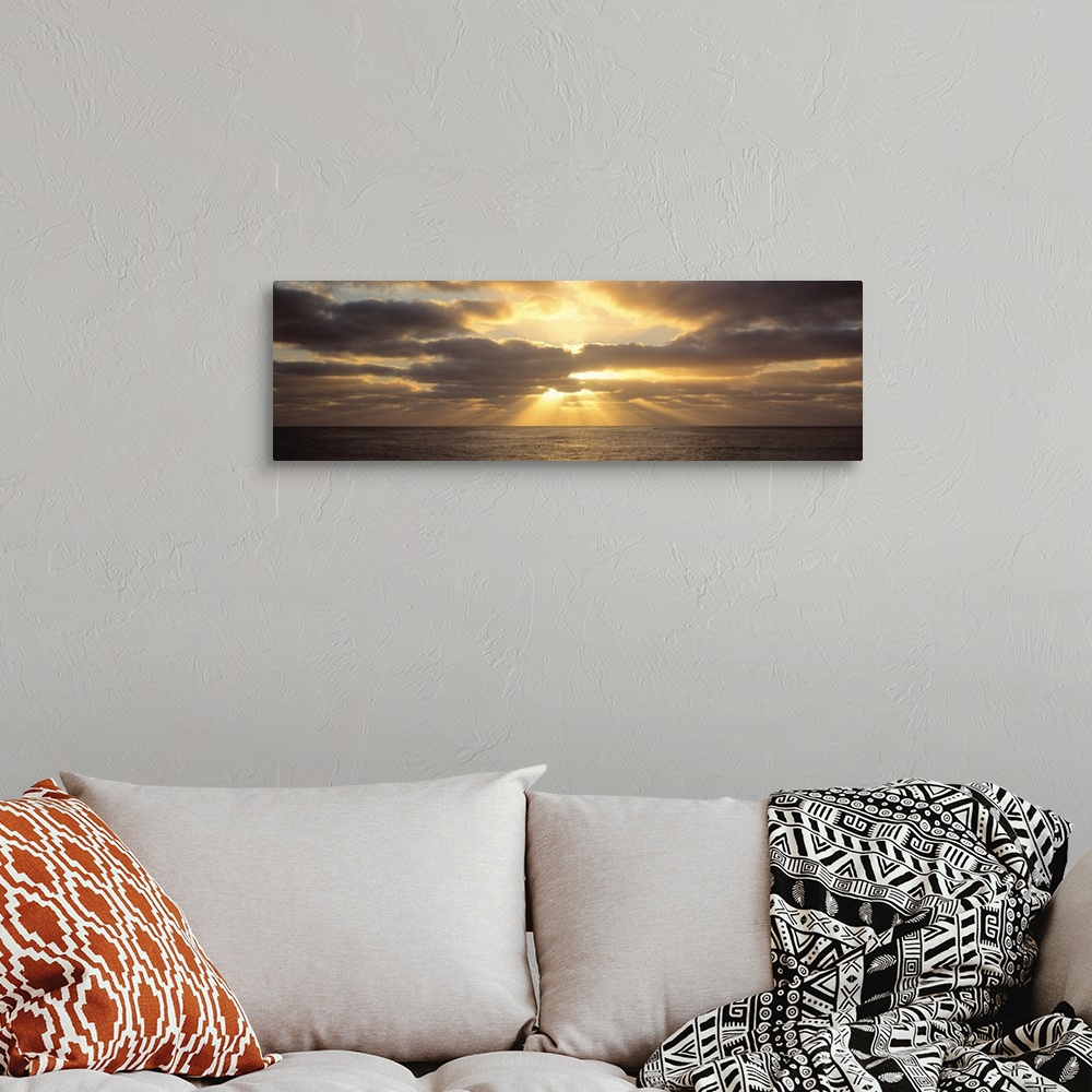 A bohemian room featuring Panoramic photograph on a big canvas of a sunset beaming through large clouds, over the water in ...