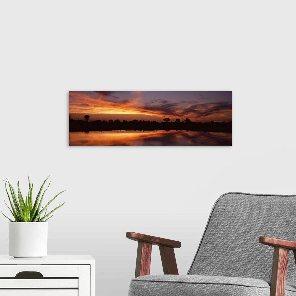 A modern room featuring Panoramic photo on canvas of a bright sunset along a river in Africa with a tree line silhouetted...