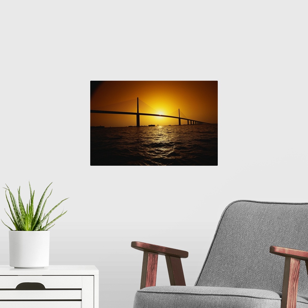 A modern room featuring Setting sun framed by the two towers of the Sunshine Skyway bridge, a concrete cable-stayed struc...