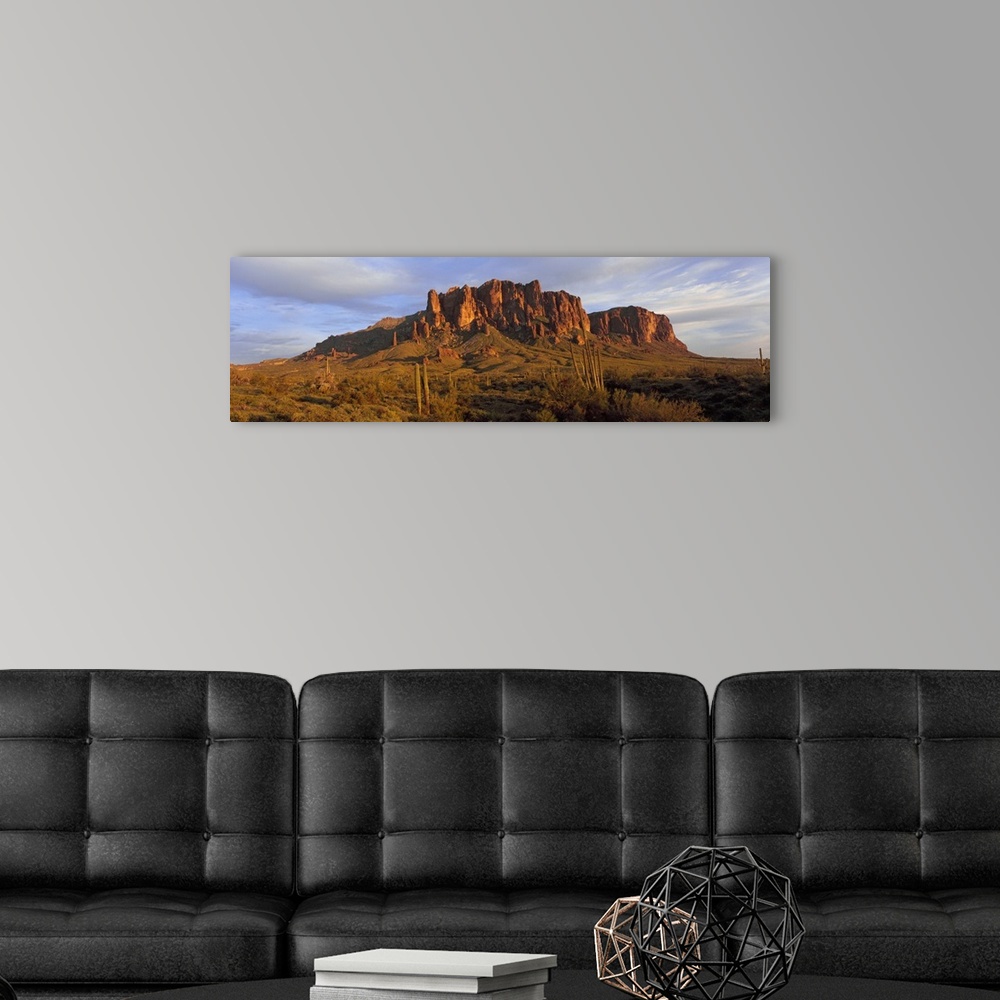 A modern room featuring An immense rock formation is photographed from a distance with green land in front of it that is ...