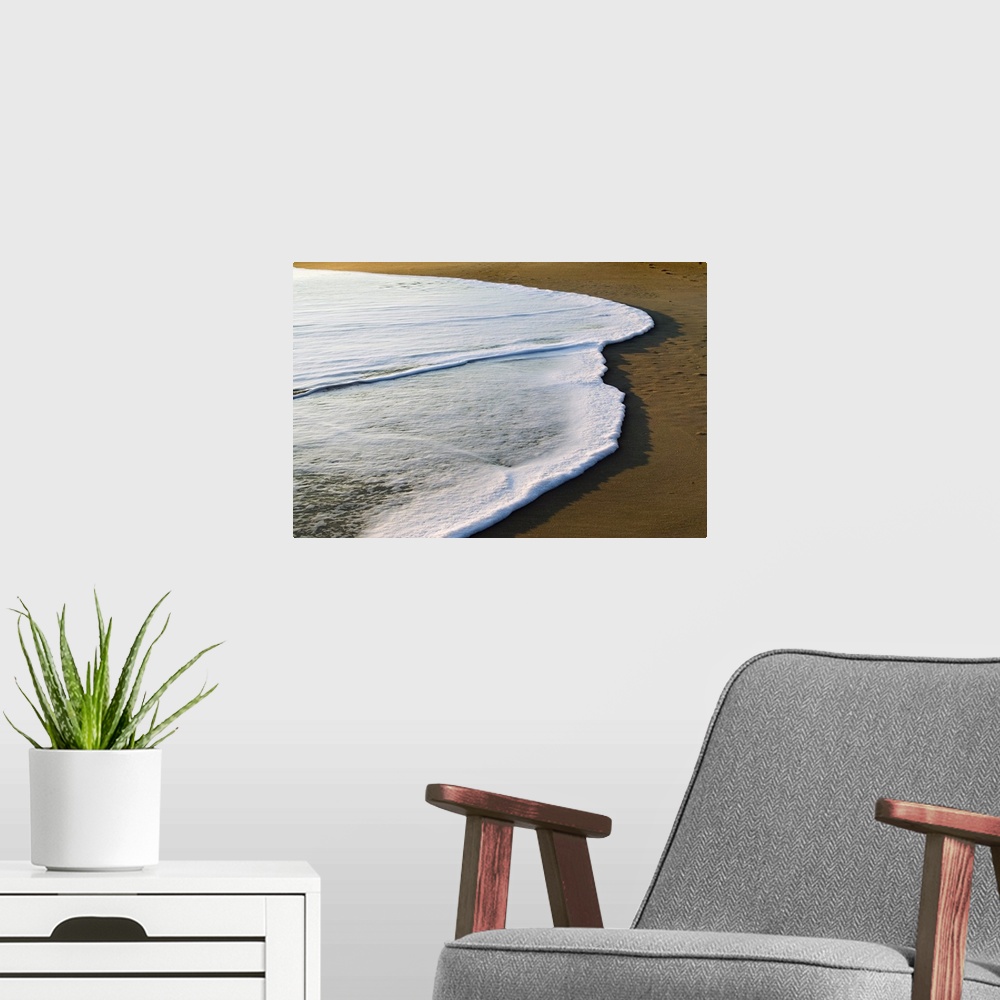 A modern room featuring Horizontal, large photograph of the white surf covering part of the sand on a beach of the Outer ...