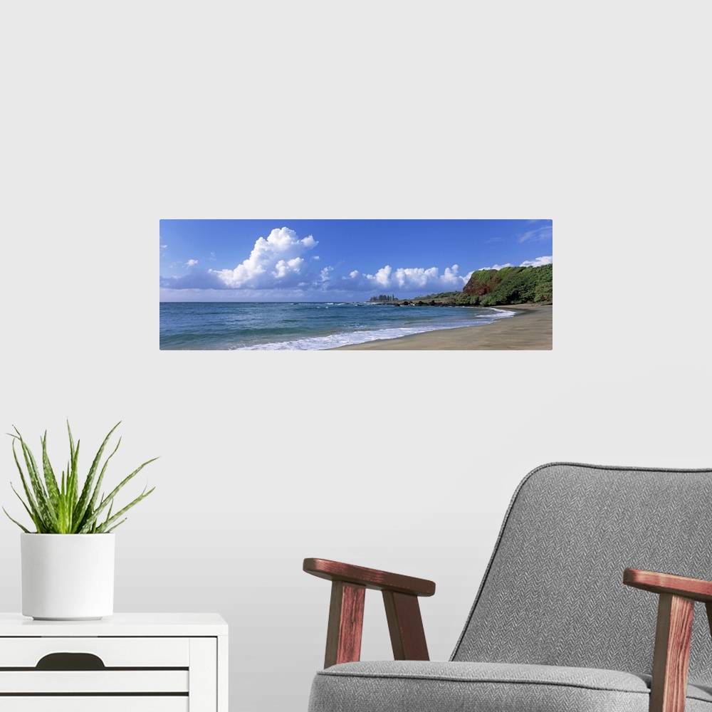 A modern room featuring Horizontal photograph on a giant wall hanging of the shoreline along Hamoa Beach, green hills in ...