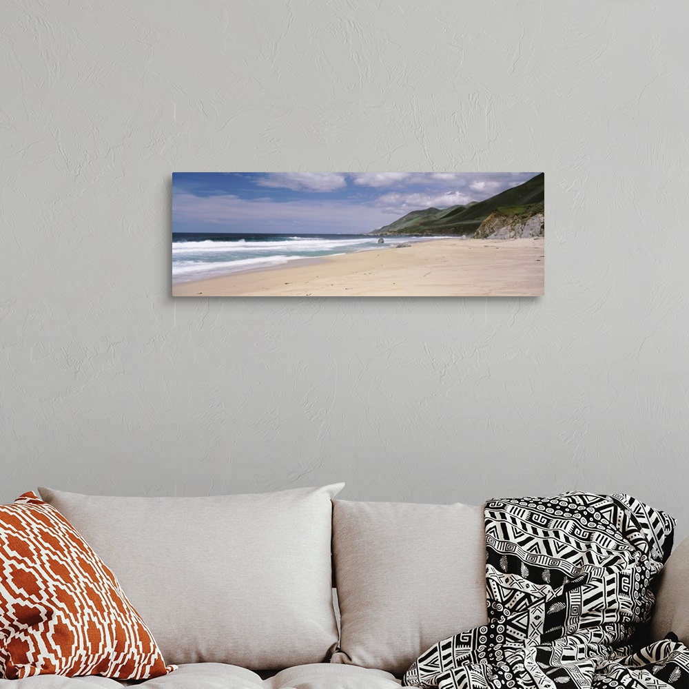 A bohemian room featuring Panoramic photograph of shoreline with mountains.  There are waves rolling in under a cloudy sky.