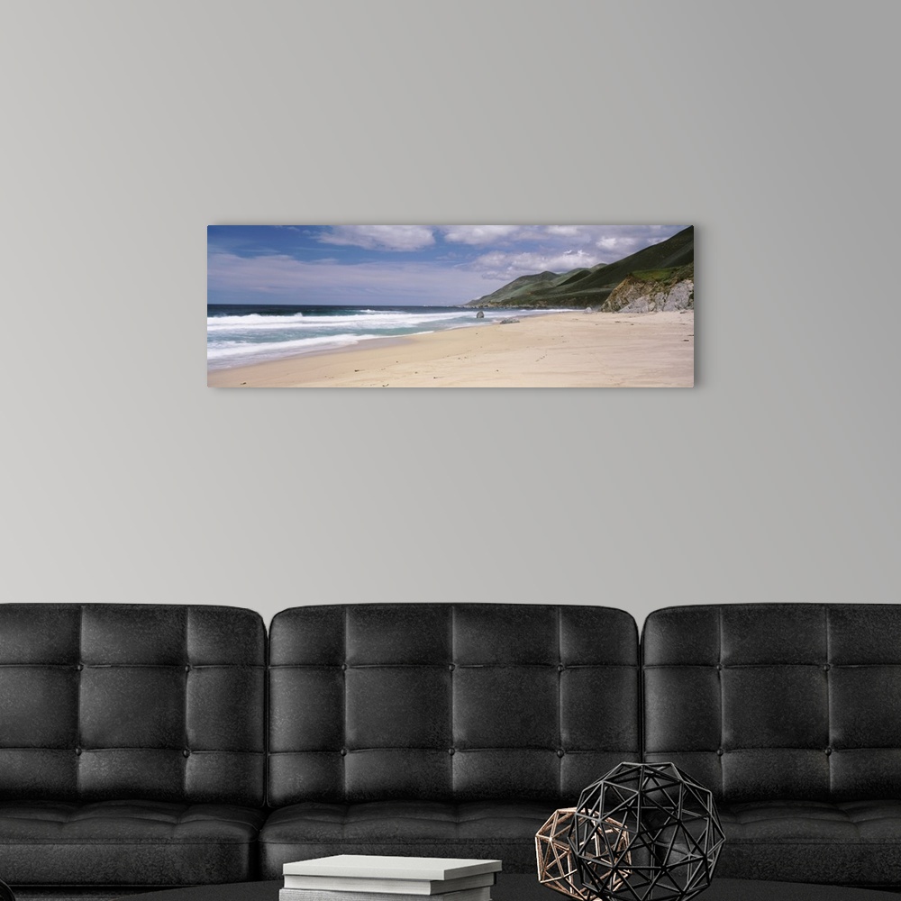 A modern room featuring Panoramic photograph of shoreline with mountains.  There are waves rolling in under a cloudy sky.