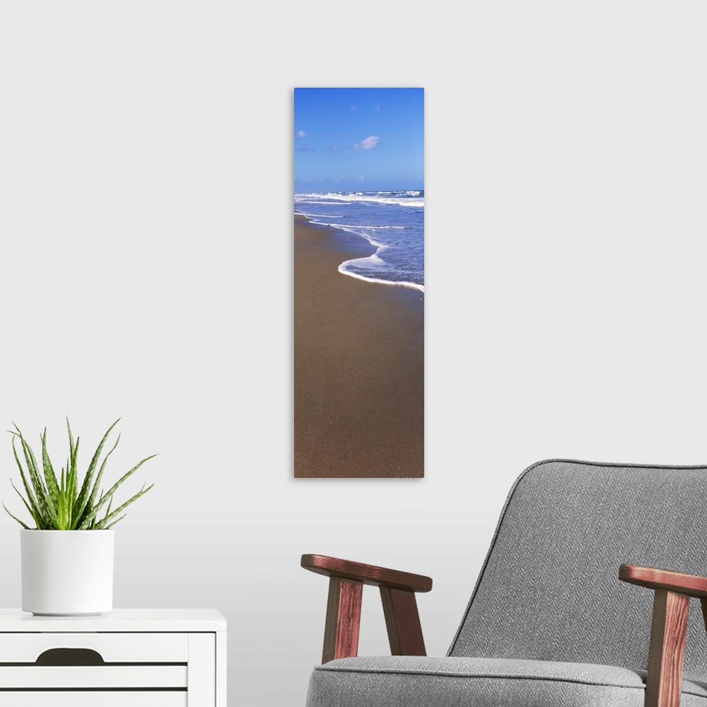 A modern room featuring A tall panoramic piece of the ocean water rushing up onto the dark sand.