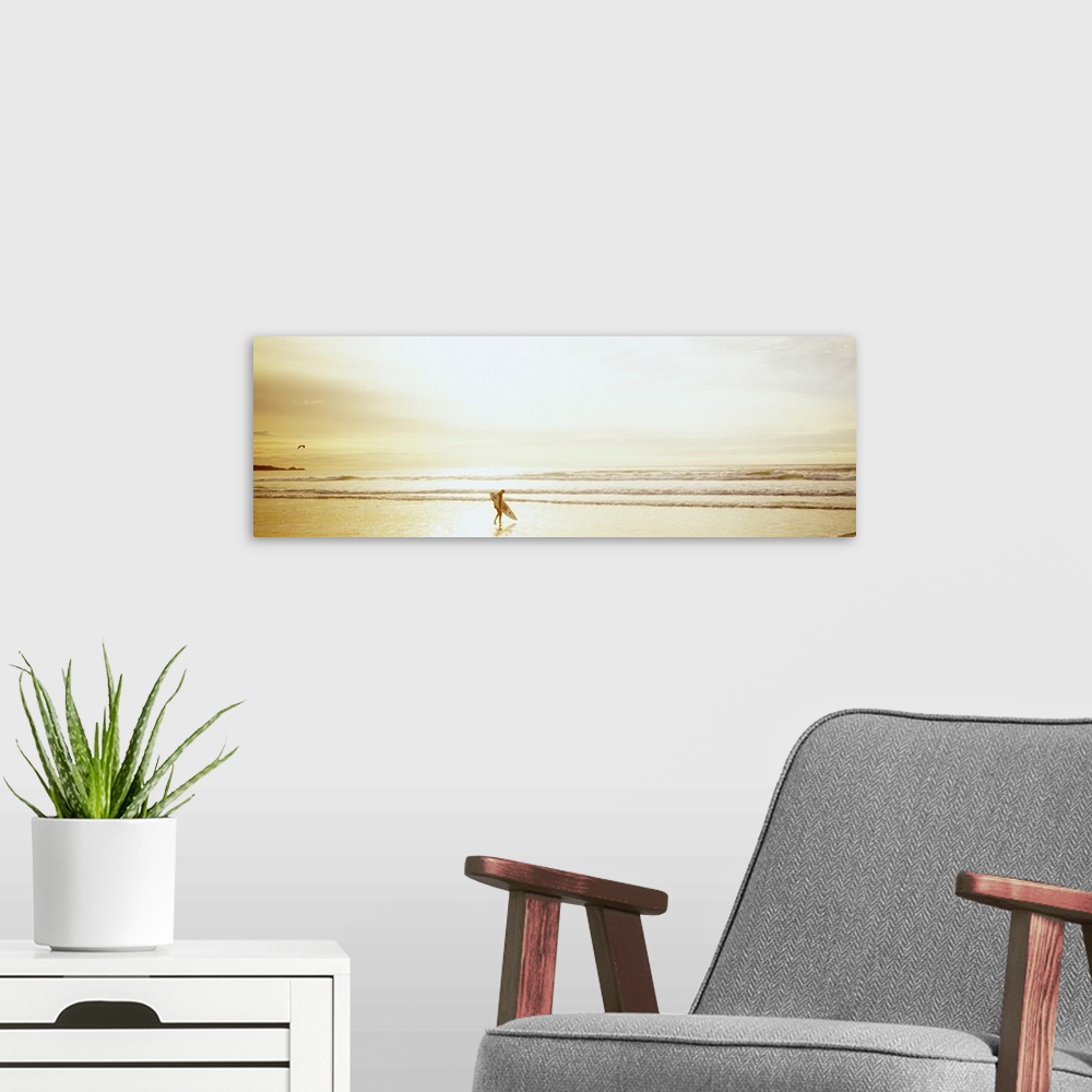 A modern room featuring Wide angle photograph of a lone surfer carrying a surf board along Ocean Beach as the tide rolls ...