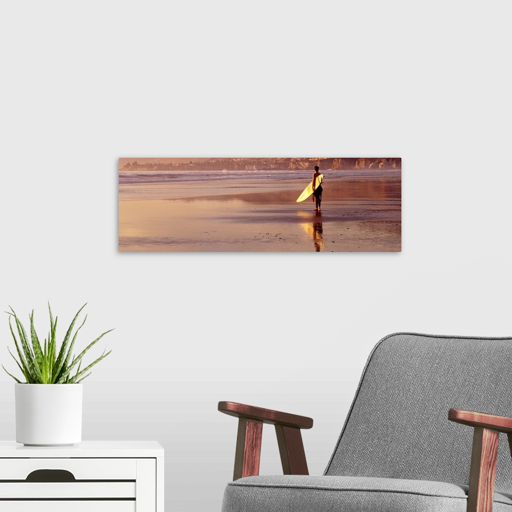 A modern room featuring Panoramic photograph of a single surfer walking along the shore with his surfboard at Pismo Beach...