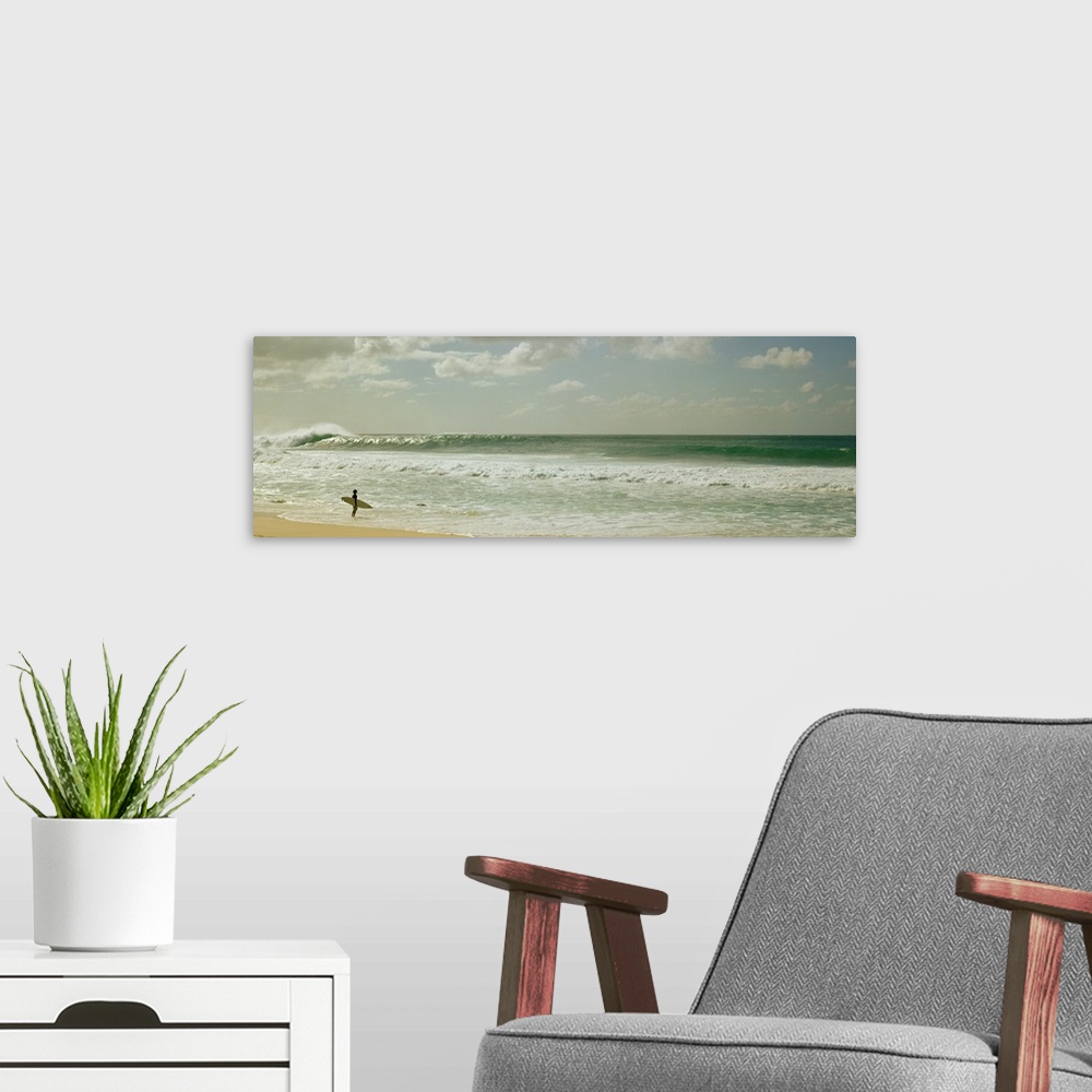 A modern room featuring Panoramic image of a surfer standing where the ocean meets the beach shore looking at a big wave ...