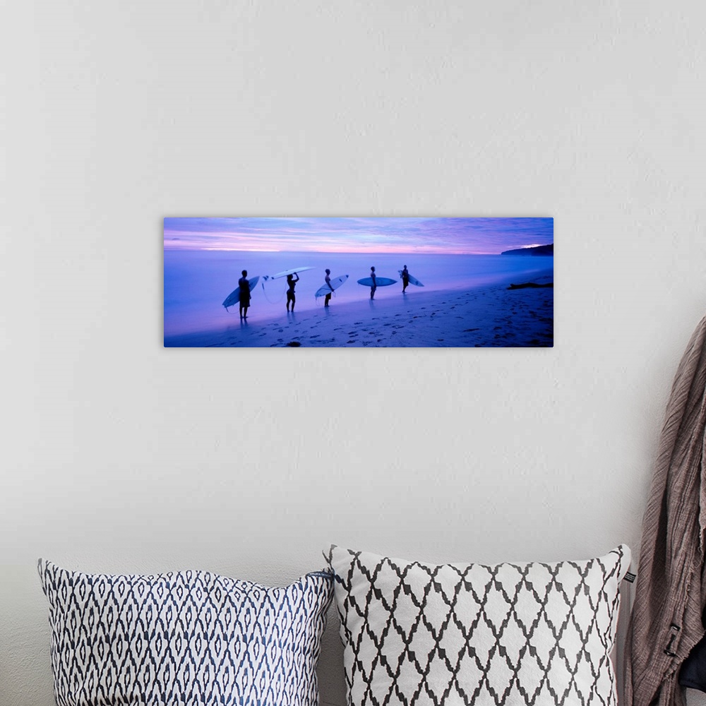 A bohemian room featuring Panoramic photograph shows a group of five surfboarders walking along a sandy shoreline under dim...