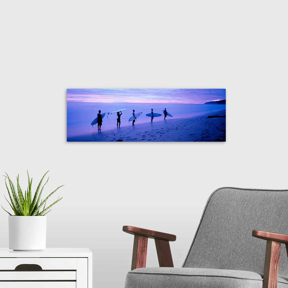 A modern room featuring Panoramic photograph shows a group of five surfboarders walking along a sandy shoreline under dim...