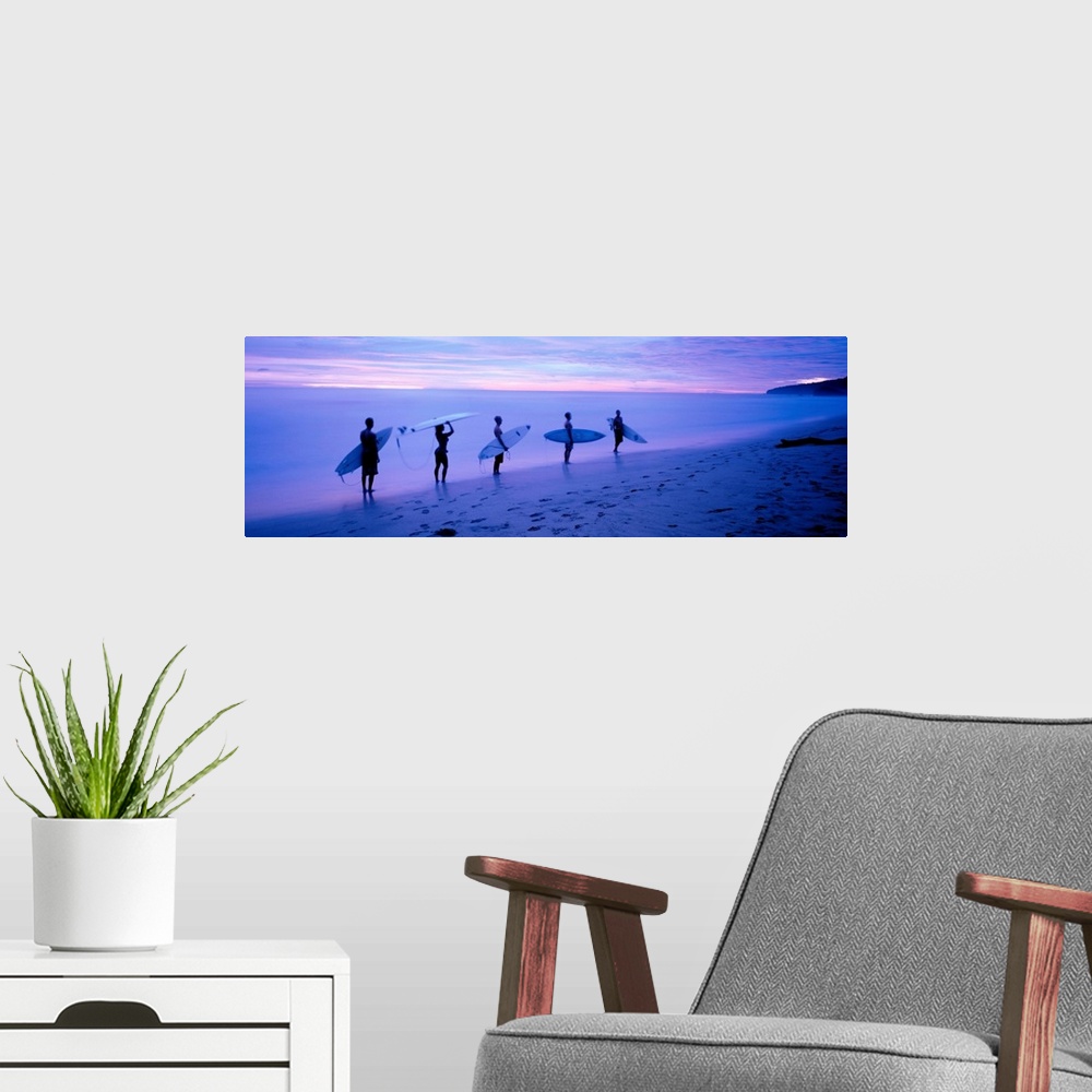 A modern room featuring Panoramic photograph shows a group of five surfboarders walking along a sandy shoreline under dim...