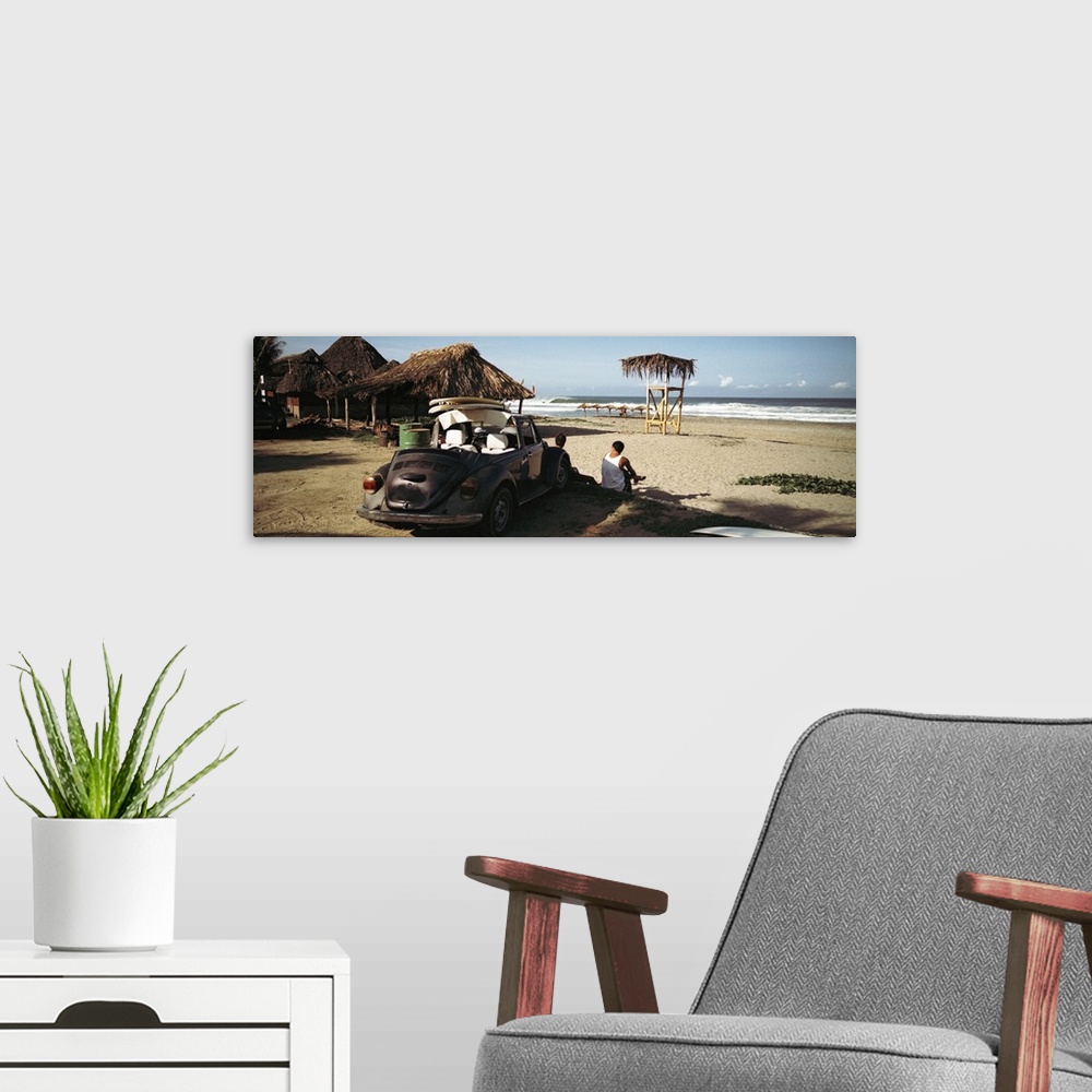 A modern room featuring A big panoramic photograph of surfers sitting in front of their car looking out at the ocean. Sma...