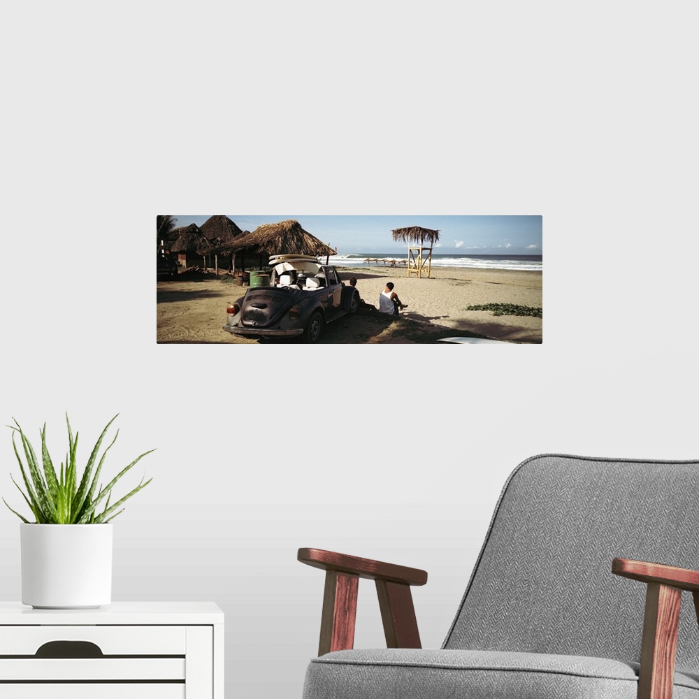 A modern room featuring A big panoramic photograph of surfers sitting in front of their car looking out at the ocean. Sma...
