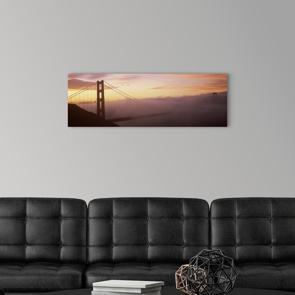 A modern room featuring Panoramic photo on canvas of the silhouette of the Golden Gate Bridge coming out of the fog at su...