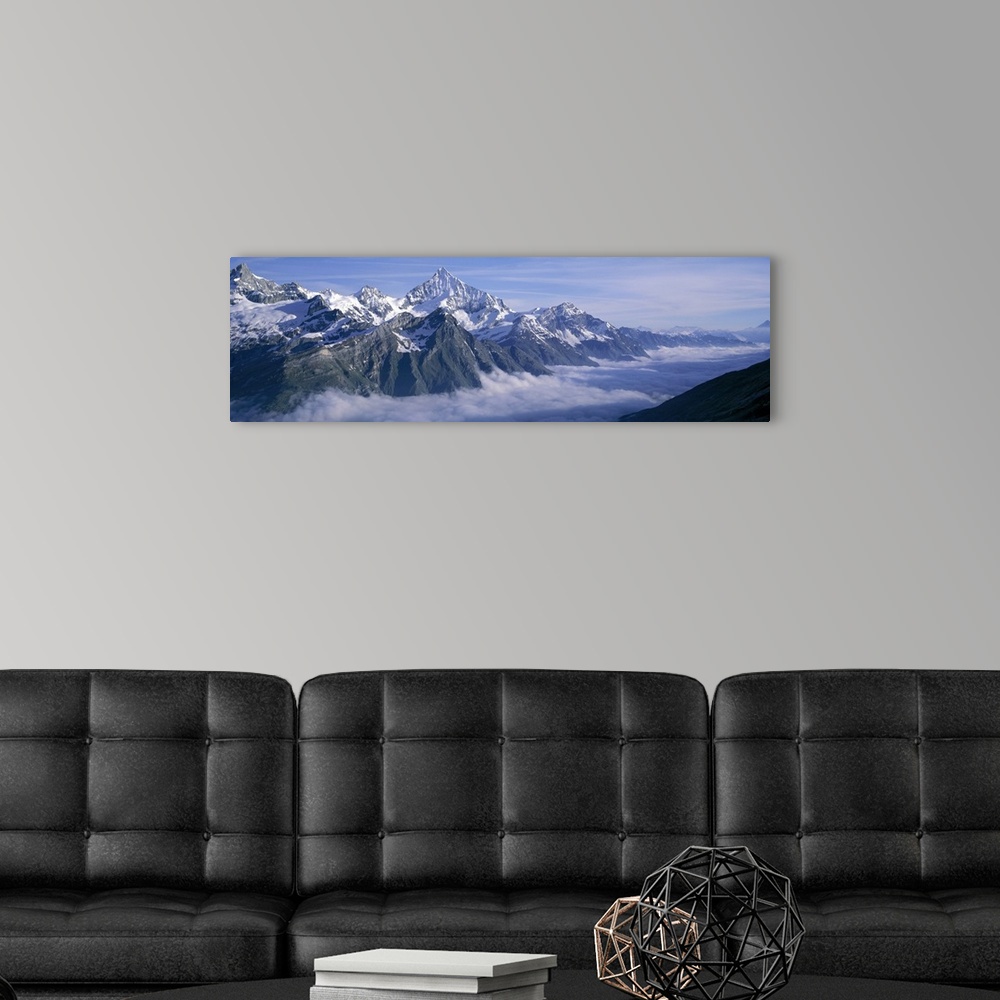 A modern room featuring Panoramic, aerial photograph of thick clouds surrounding the snow capped Swiss Alps, against a bl...