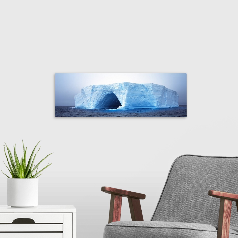 A modern room featuring This panoramic photograph is of an immense iceberg that has a tunnel going through the middle of it.