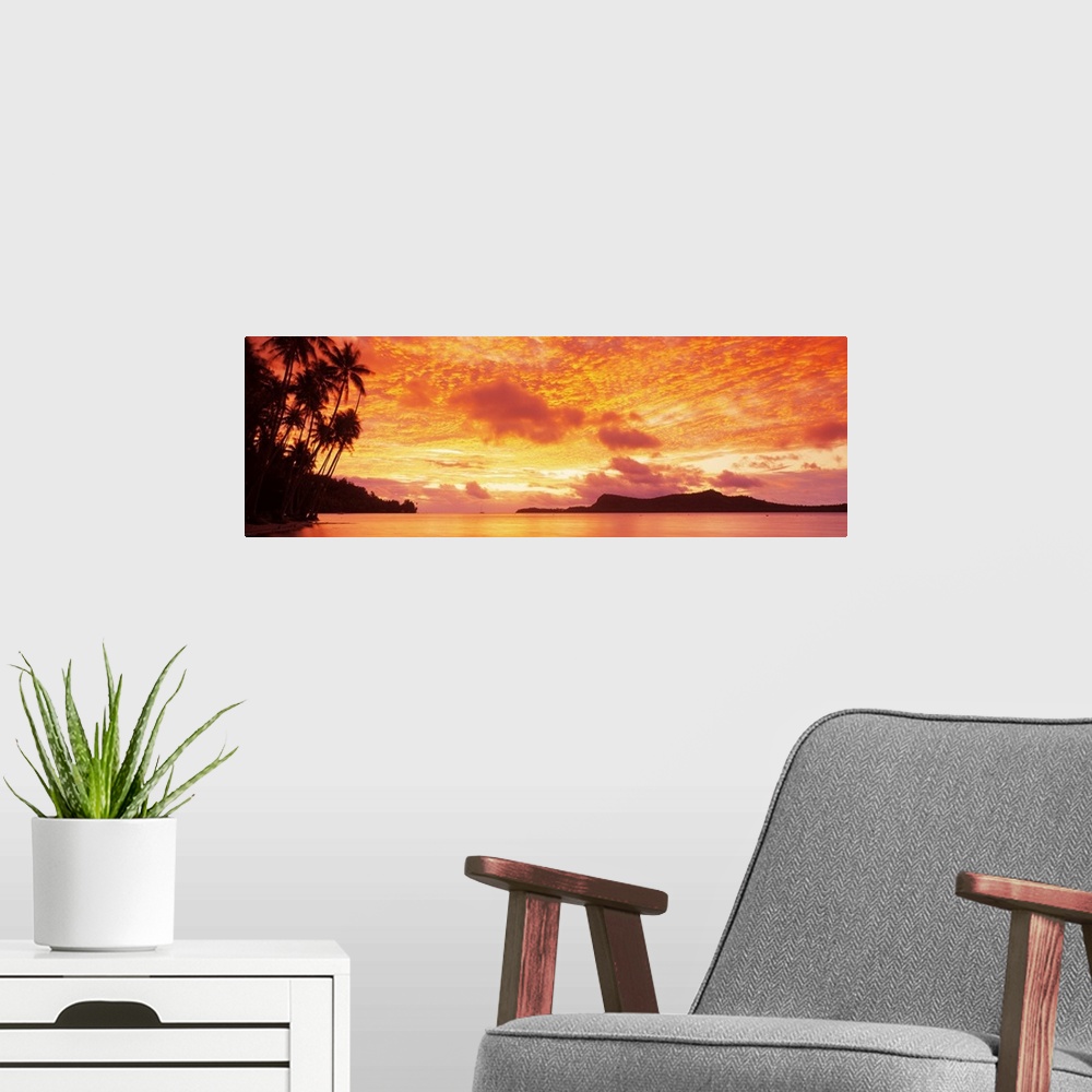 A modern room featuring Panoramic photograph includes a vivid sunset over a beach filled with palm trees.  In the backgro...