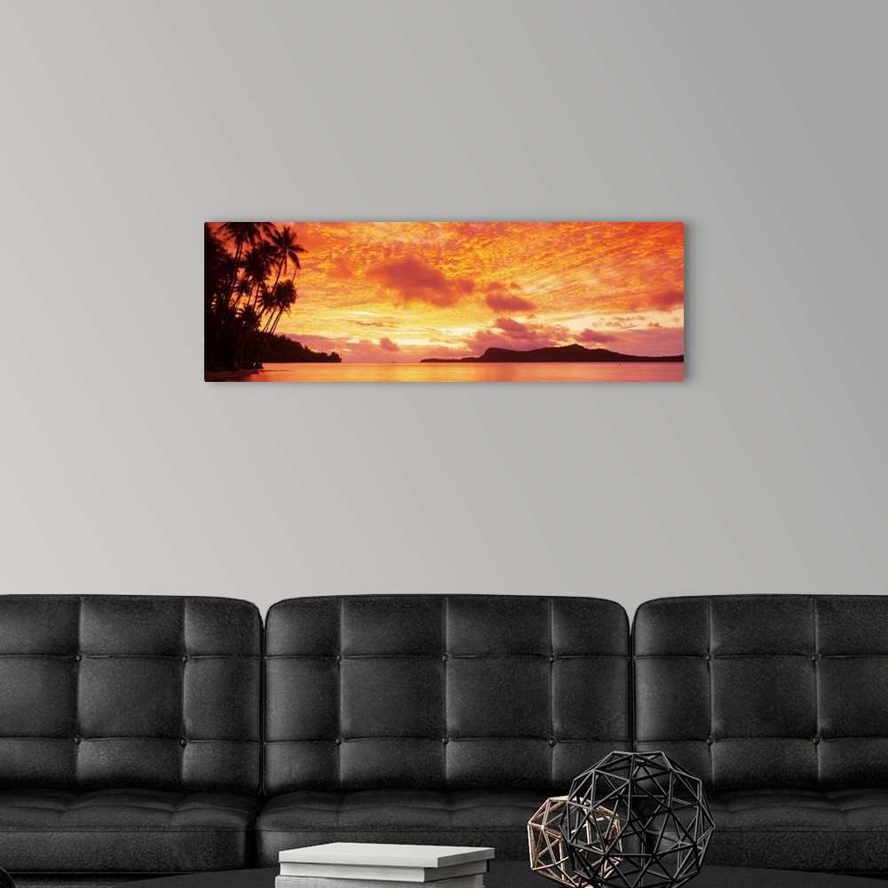 A modern room featuring Panoramic photograph includes a vivid sunset over a beach filled with palm trees.  In the backgro...