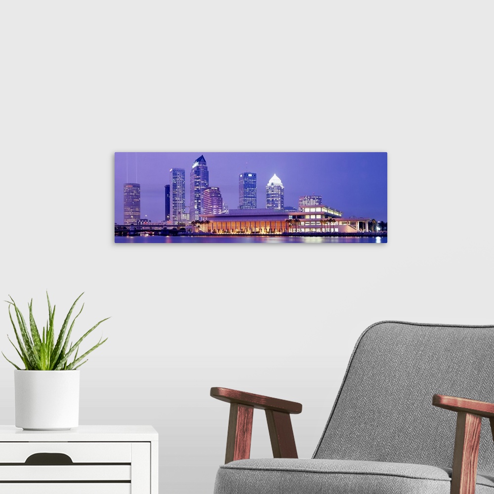 A modern room featuring The Tampa skyline is photographed in panoramic view during the night with the buildings all illum...