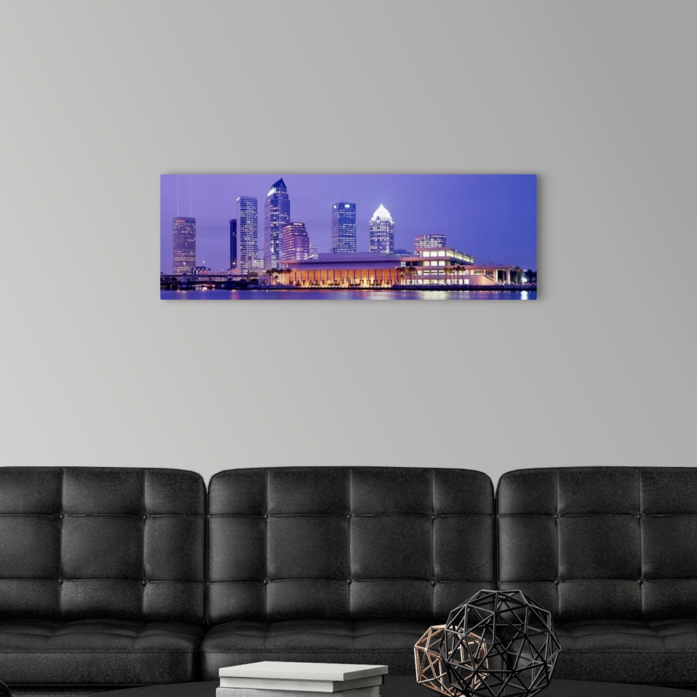 A modern room featuring The Tampa skyline is photographed in panoramic view during the night with the buildings all illum...