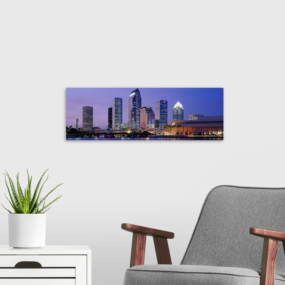 A modern room featuring Wide angle photograph of the Tampa skyline in front a vivid sky, lit up at night and reflecting i...