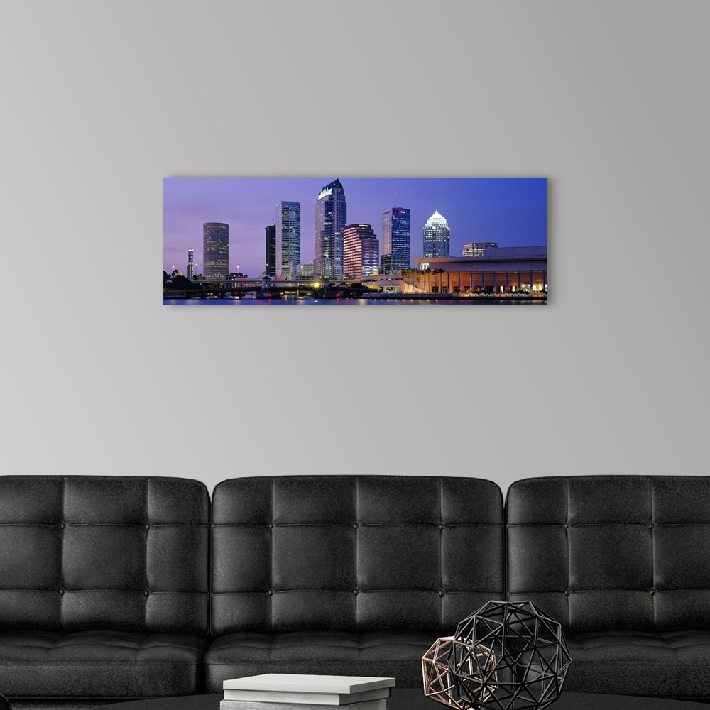A modern room featuring Wide angle photograph of the Tampa skyline in front a vivid sky, lit up at night and reflecting i...