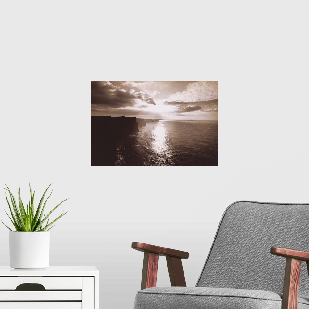 A modern room featuring This big artwork piece is of a sepia toned sunset reflecting in the ocean water below with immens...