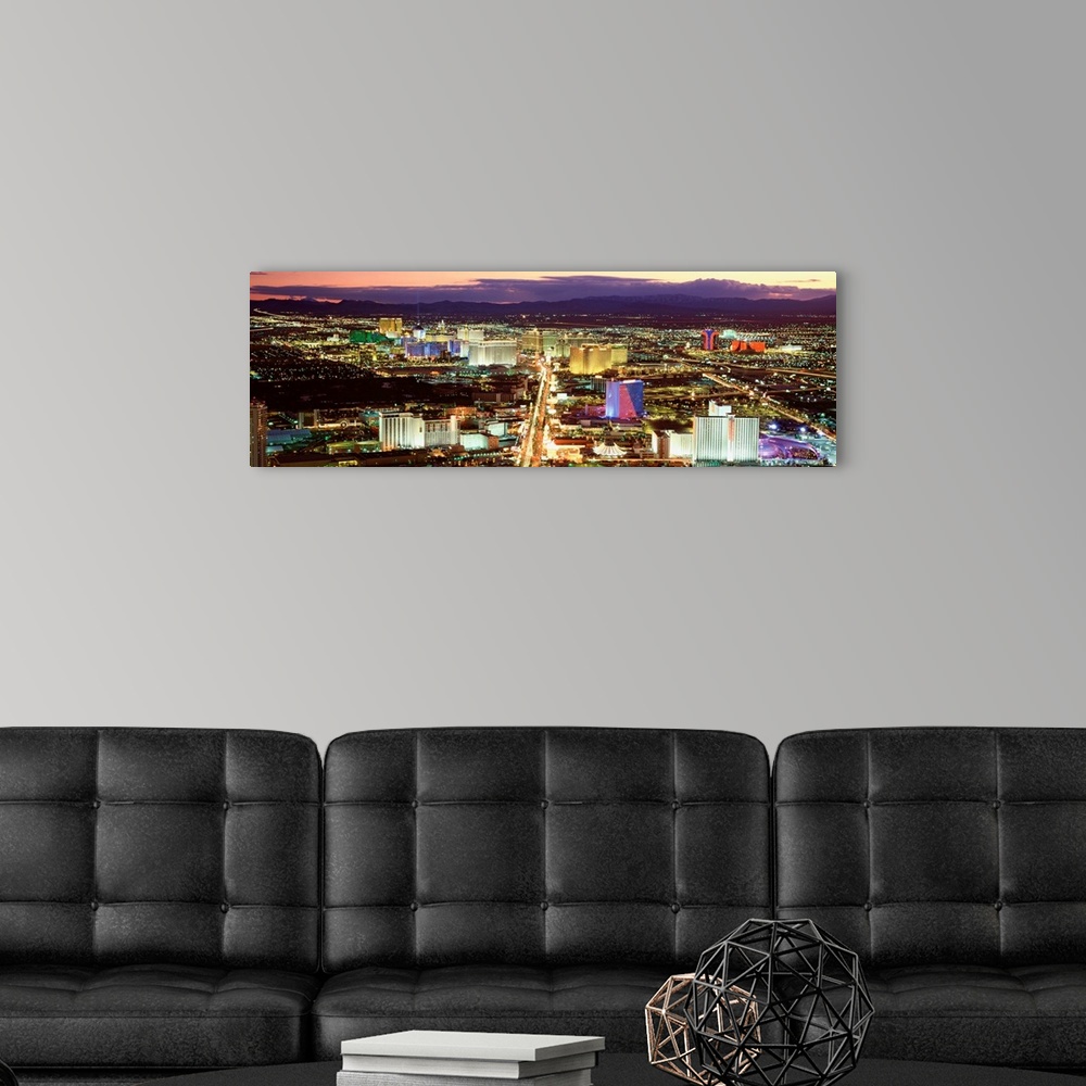A modern room featuring This wall art is a panoramic photograph taken from high in the air of the Sin cityos night lights...