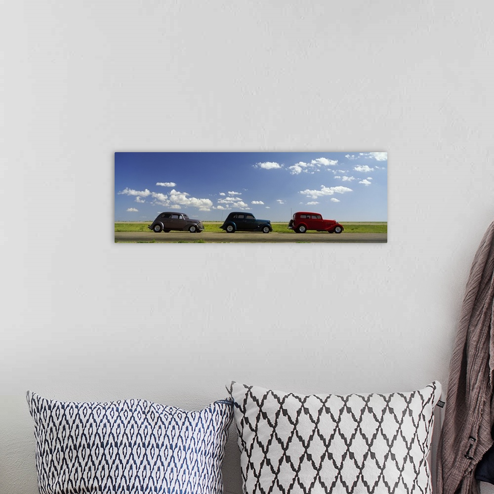 A bohemian room featuring Panoramic photograph of three vintage cars driving down the street under cloudy skies.