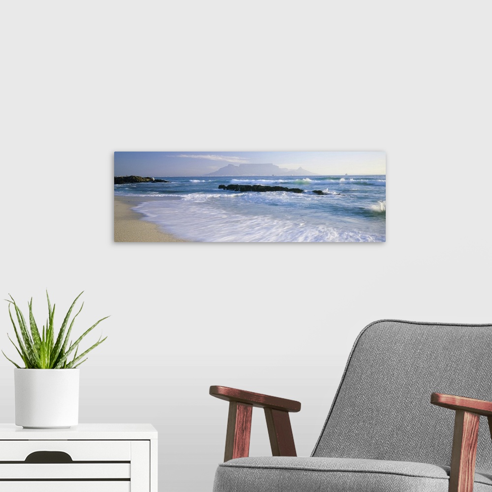 A modern room featuring Panoramic photograph taken of the ocean with waves crashing and rushing onto the shore line. Rock...
