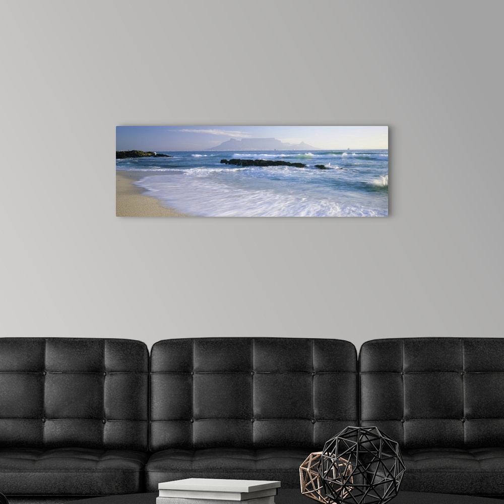 A modern room featuring Panoramic photograph taken of the ocean with waves crashing and rushing onto the shore line. Rock...