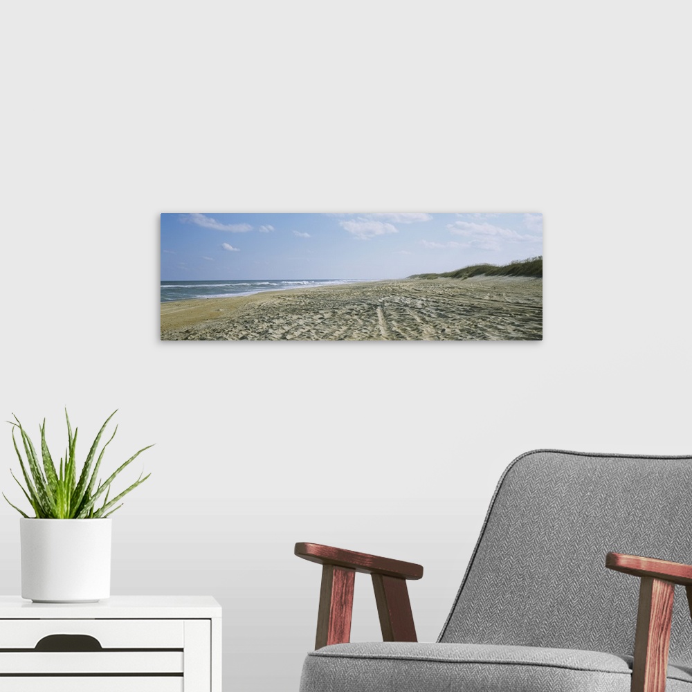 A modern room featuring A panoramic photograph of a sandy beach indented with footsteps and tracks down to the ocean water.