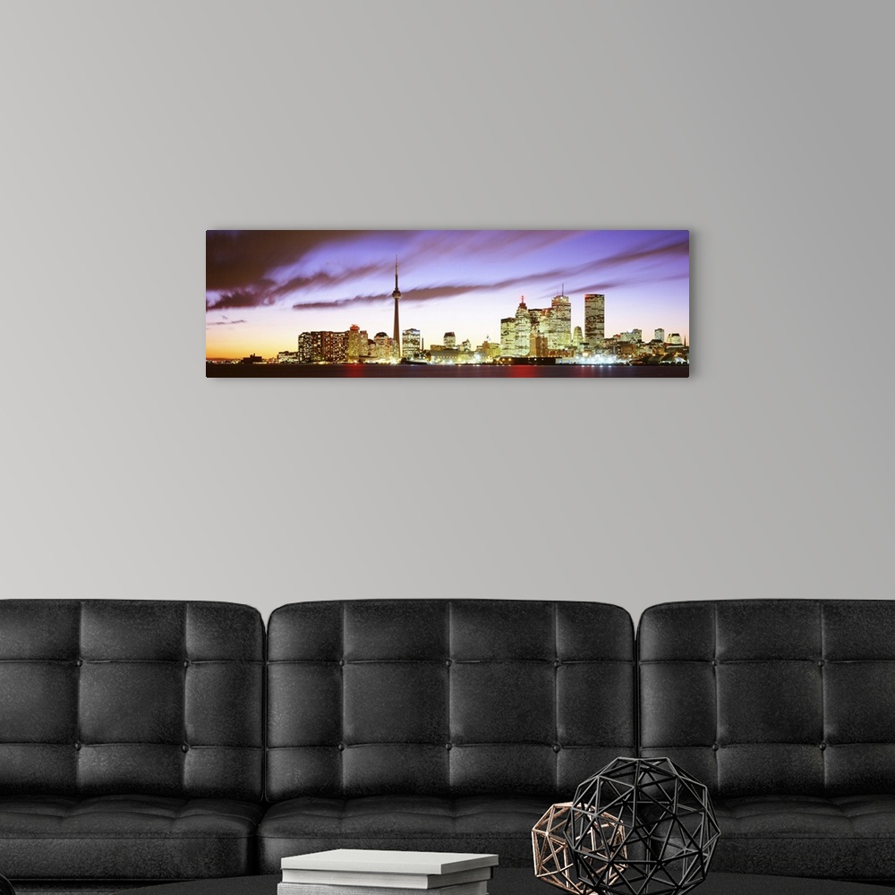 A modern room featuring Wide angle photograph of the Toronto skyline, including CN Tower, lit up at dusk, beneath whippin...