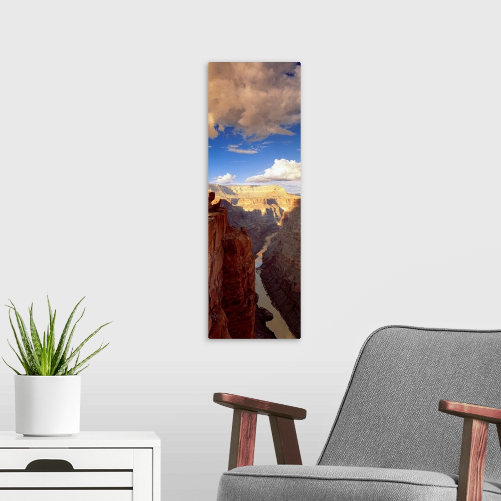 A modern room featuring Vertical panoramic photograph river running through tall rocky vertical gorge under a cloudy sky.