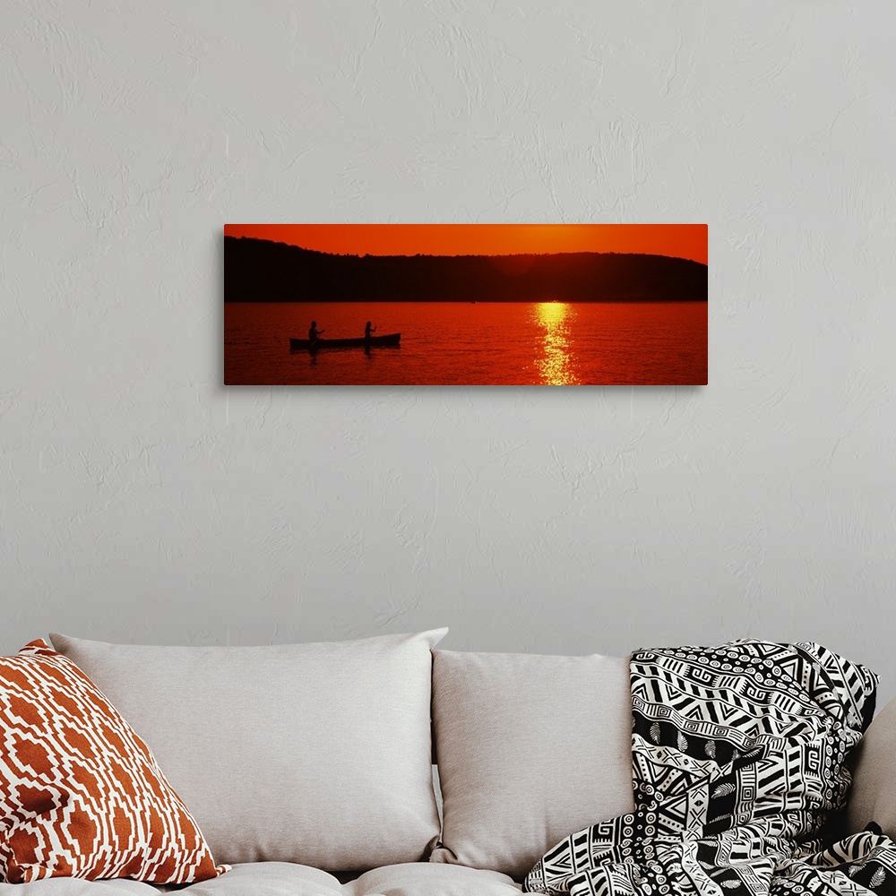 A bohemian room featuring This panoramic piece is a picture taken of two people canoeing on a lake during sunset which has ...