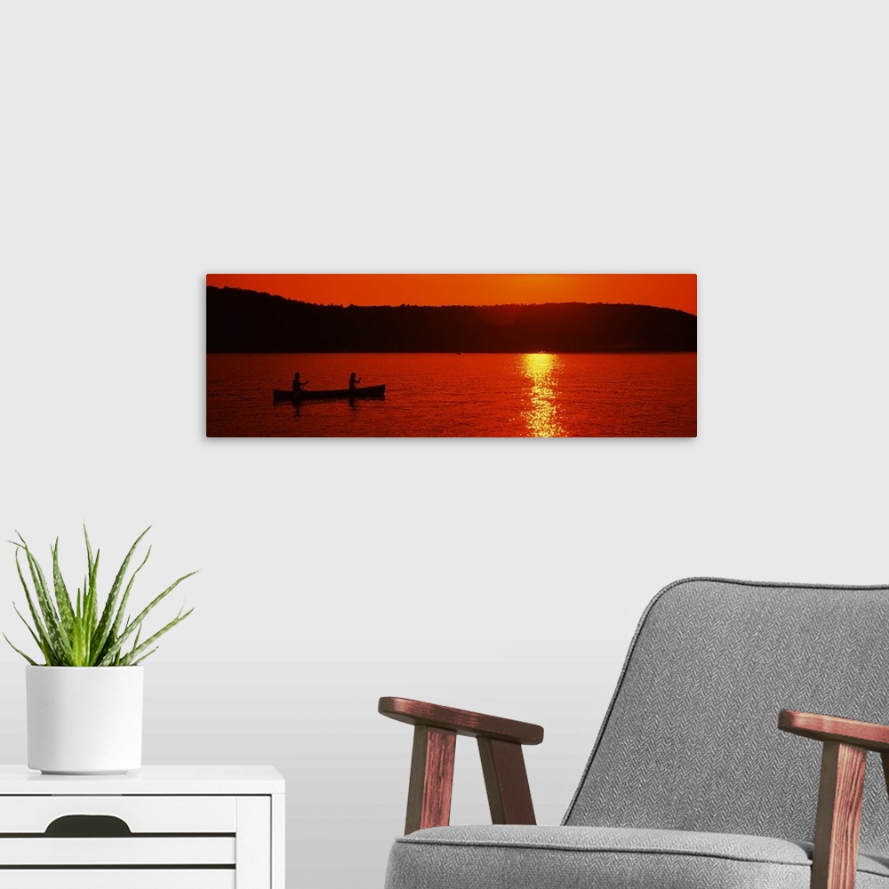 A modern room featuring This panoramic piece is a picture taken of two people canoeing on a lake during sunset which has ...
