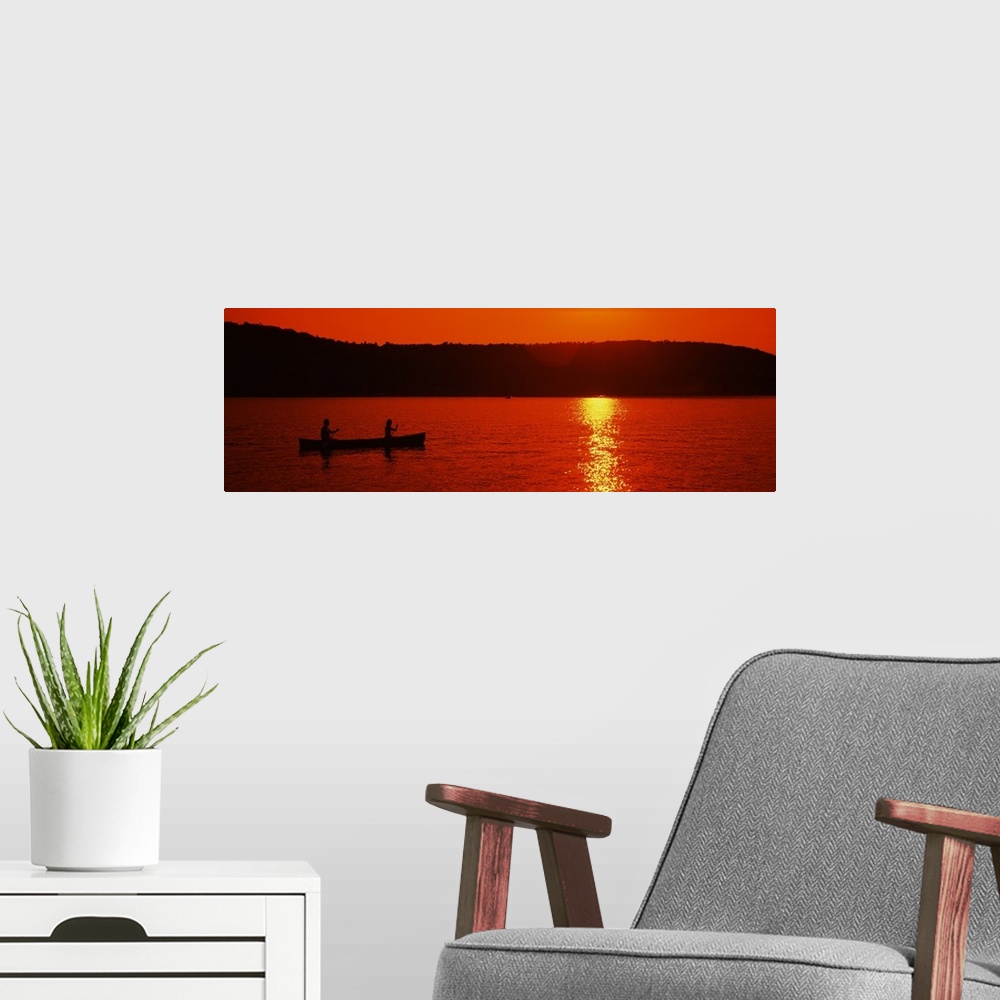 A modern room featuring This panoramic piece is a picture taken of two people canoeing on a lake during sunset which has ...
