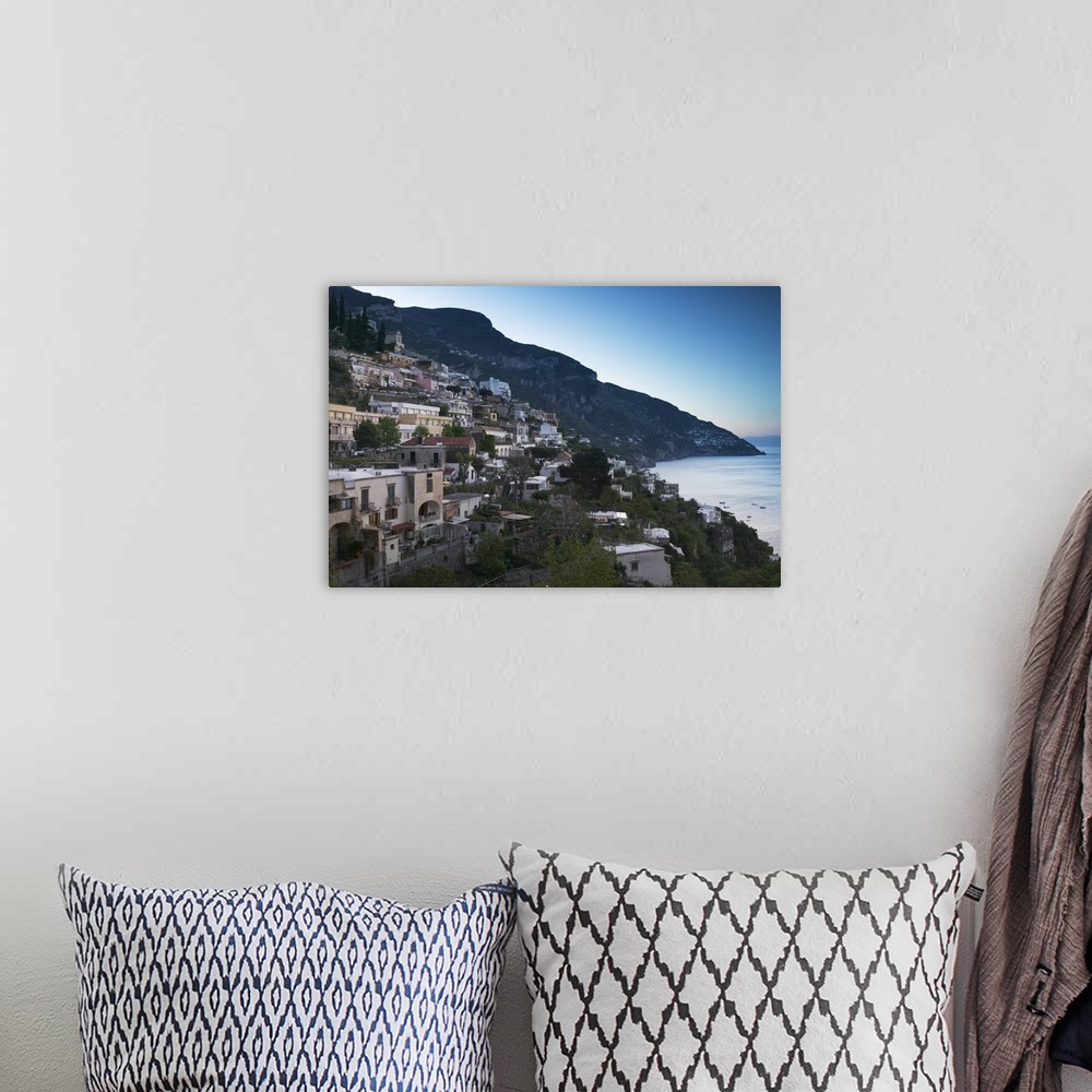 A bohemian room featuring Oversized artwork that is a picture of a town on a coast in Italy. A large hill is seen in the di...