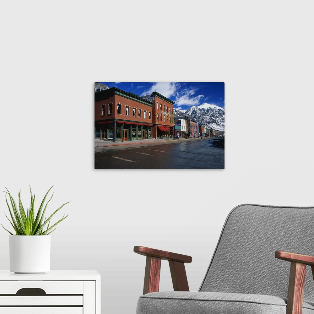 A modern room featuring Photograph of street corner lined with buildings and shops with snow covered mountains in the bac...